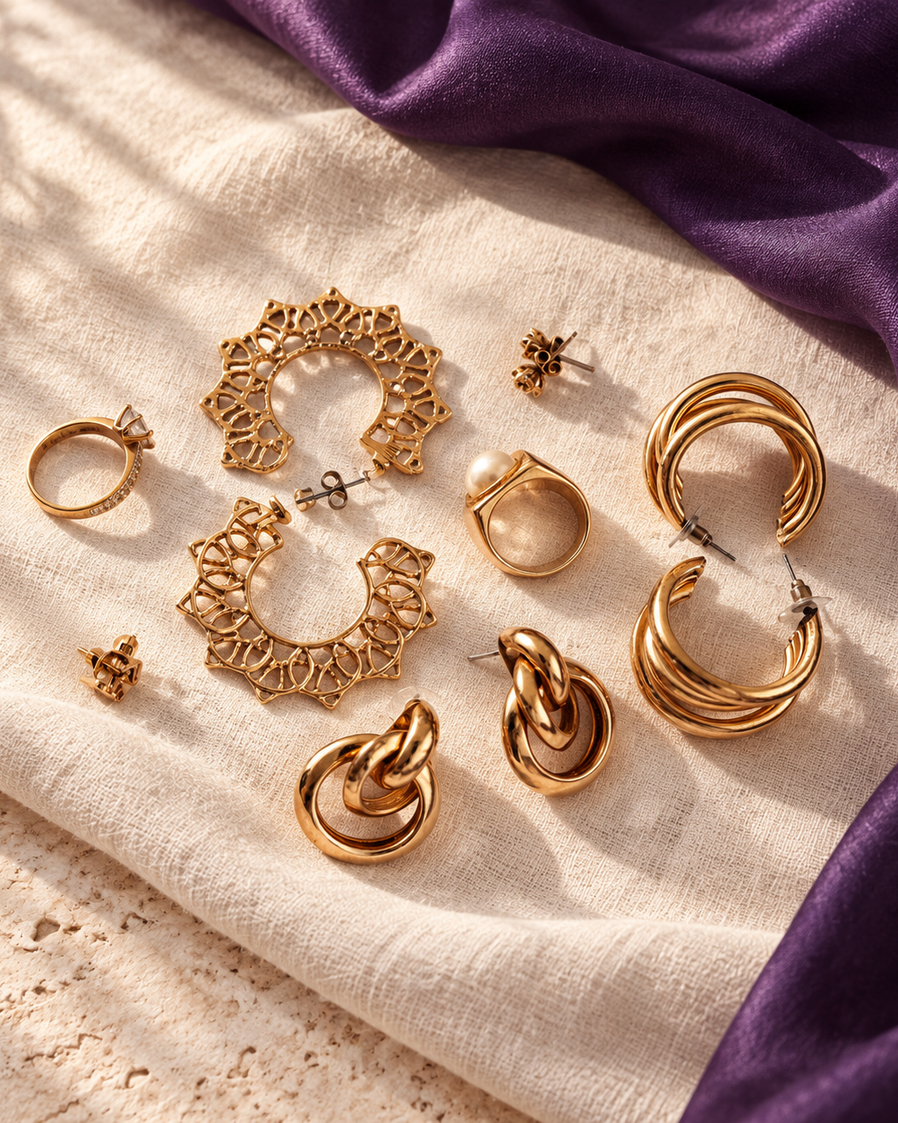Gold statement earrings and rings scattered on soft linen