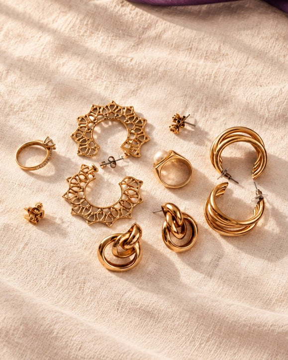 Gold statement earrings and rings scattered on soft linen