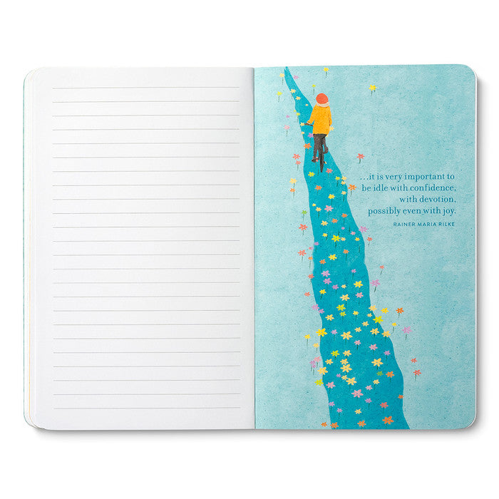 Open journal with lined pages beside a page of a small figure in yellow walking a winding blue path scattered with flowers