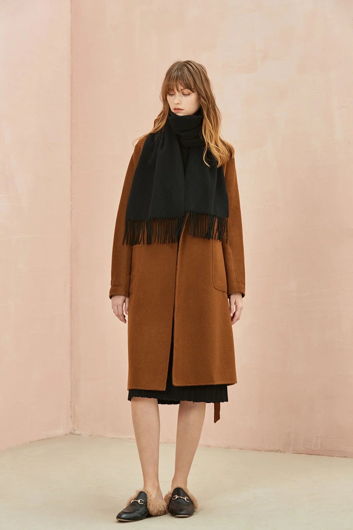 Full-length camel coat look with the Ebony black scarf, pink wall behind