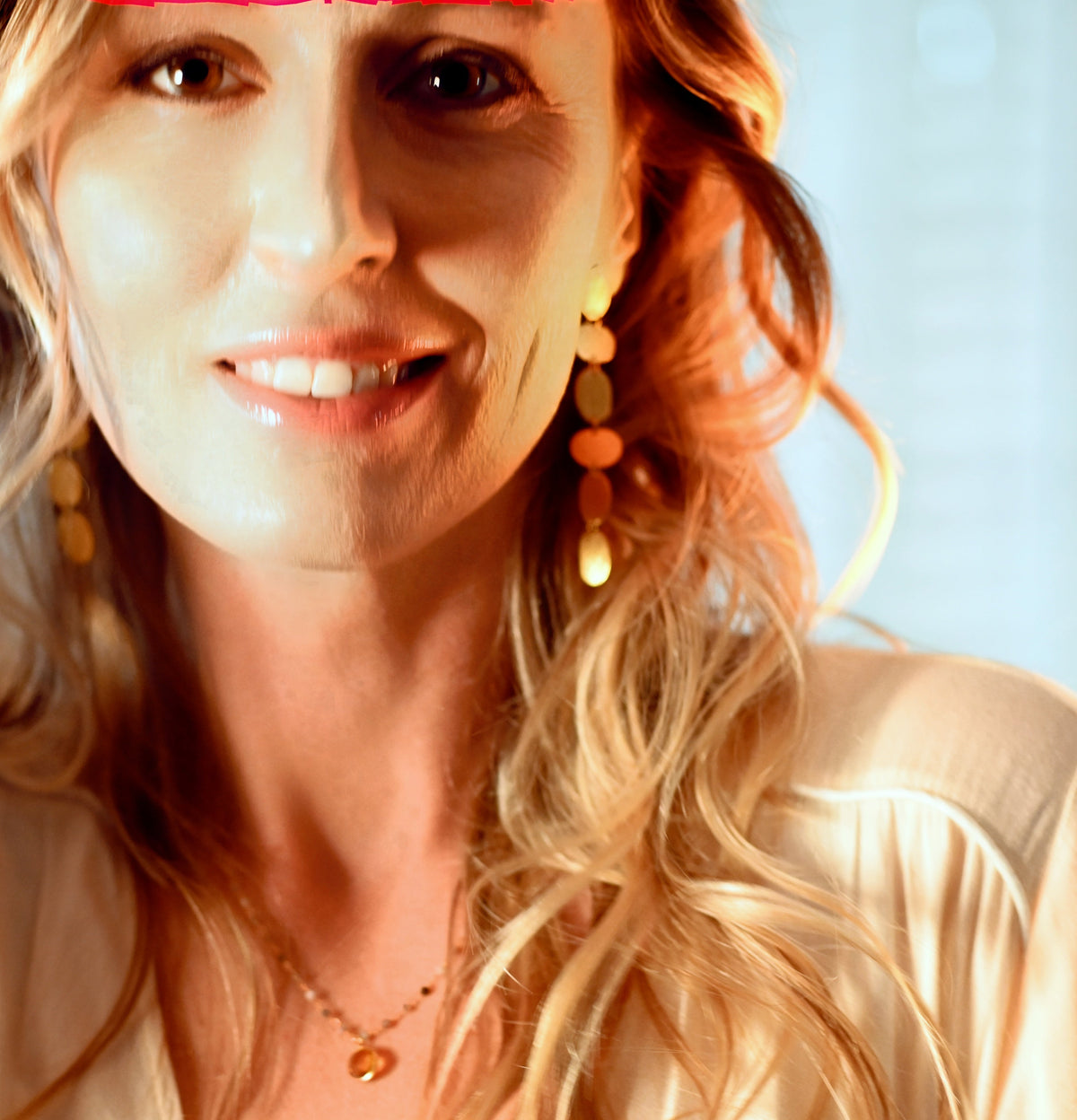 Smiling model with long strawberry-blonde hair wearing the gold linked-oval earring, in warm light