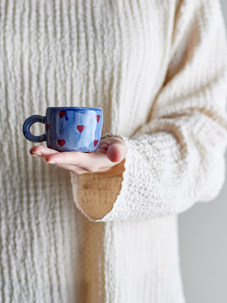 Blue heart cup held in an open hand against a cream knit sleeve