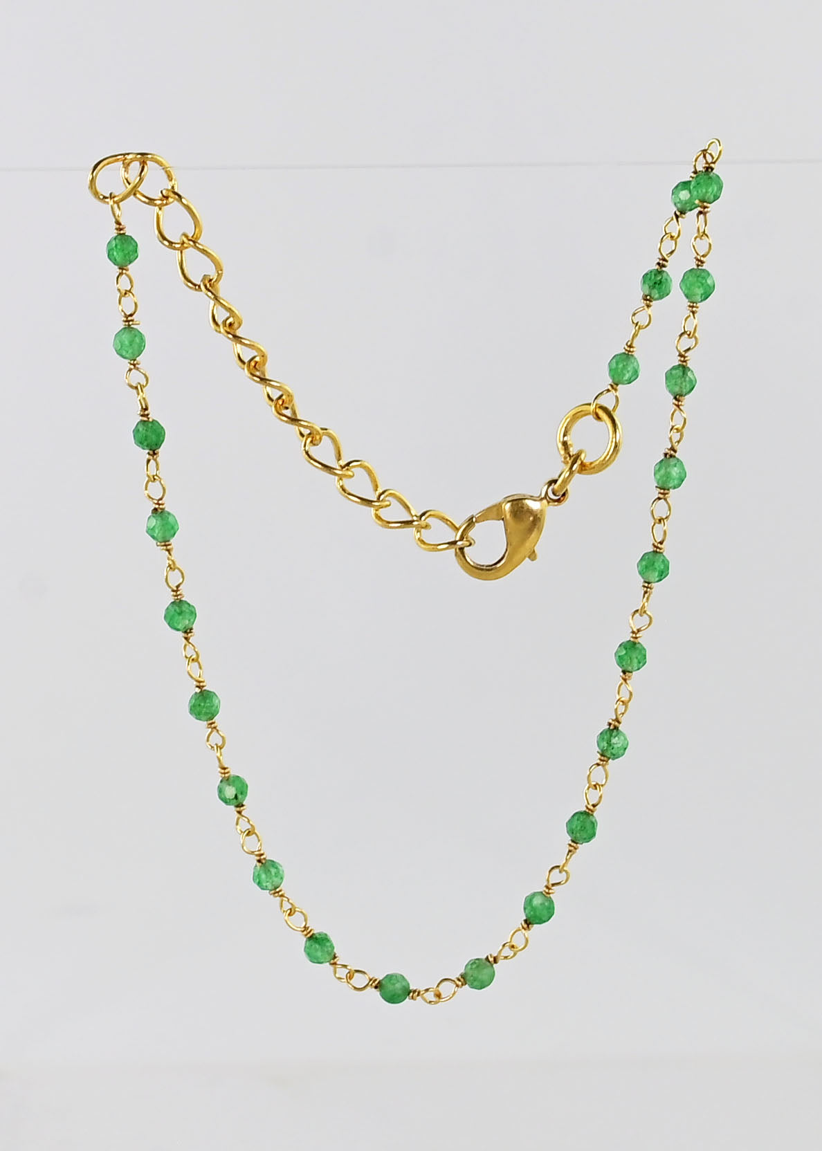 Fine gold chain bracelet with faceted green onyx beads draped on a stand
