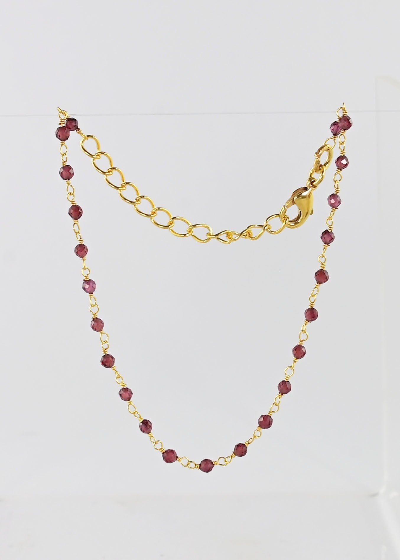 Fine gold chain bracelet with faceted garnet-red beads draped on a stand