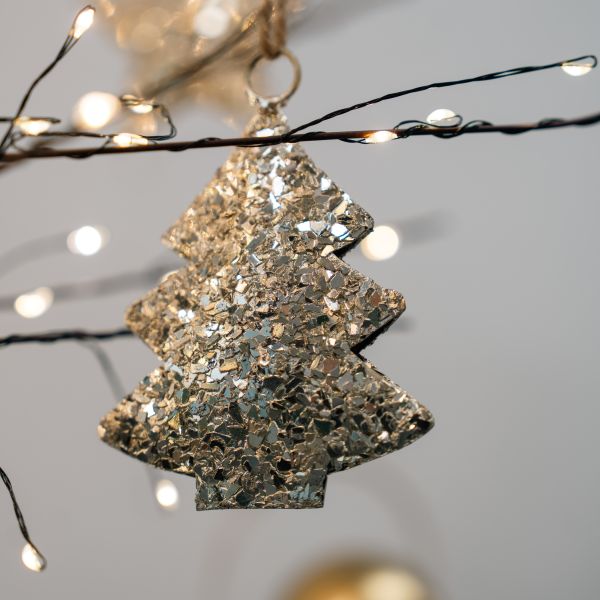Christmas tree ornament covered in chunky champagne and silver flakes, hanging from a ring among fairy lights