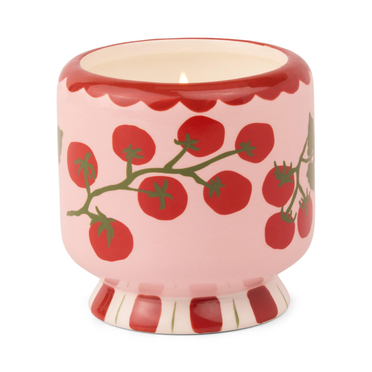Pink ceramic candle painted with red tomatoes on green vines, a red scalloped rim and a red and white striped foot, lit.