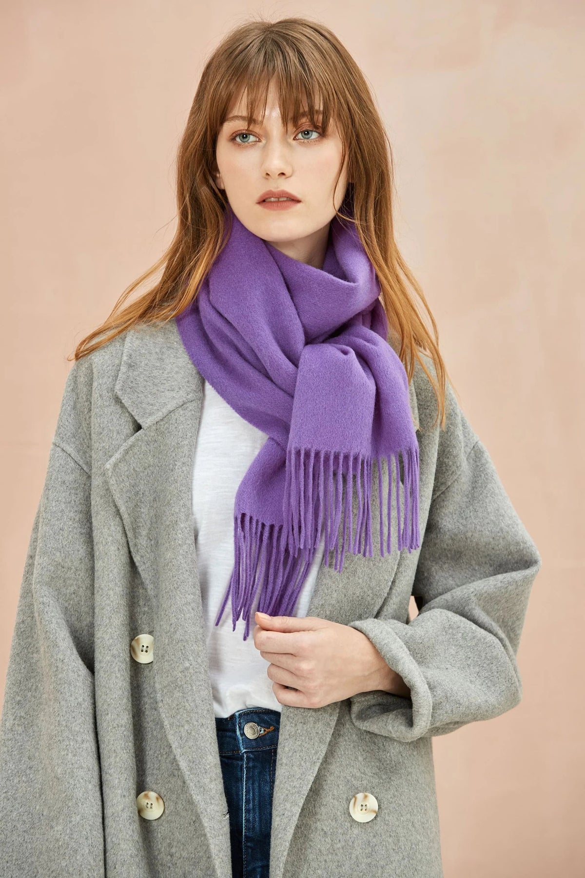 Model in a grey coat wearing the Iris violet merino scarf knotted at the front