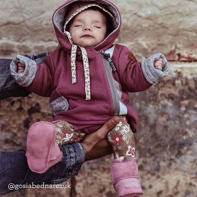 Baby in a plum hooded suit held up wearing orchid pink sheepskin booties