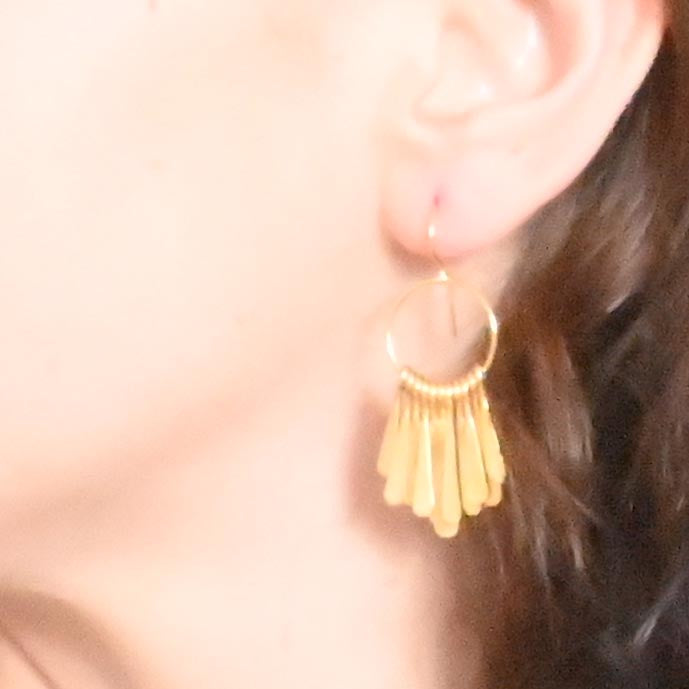Close-up of the small gold tassel hoop earring worn with dark hair