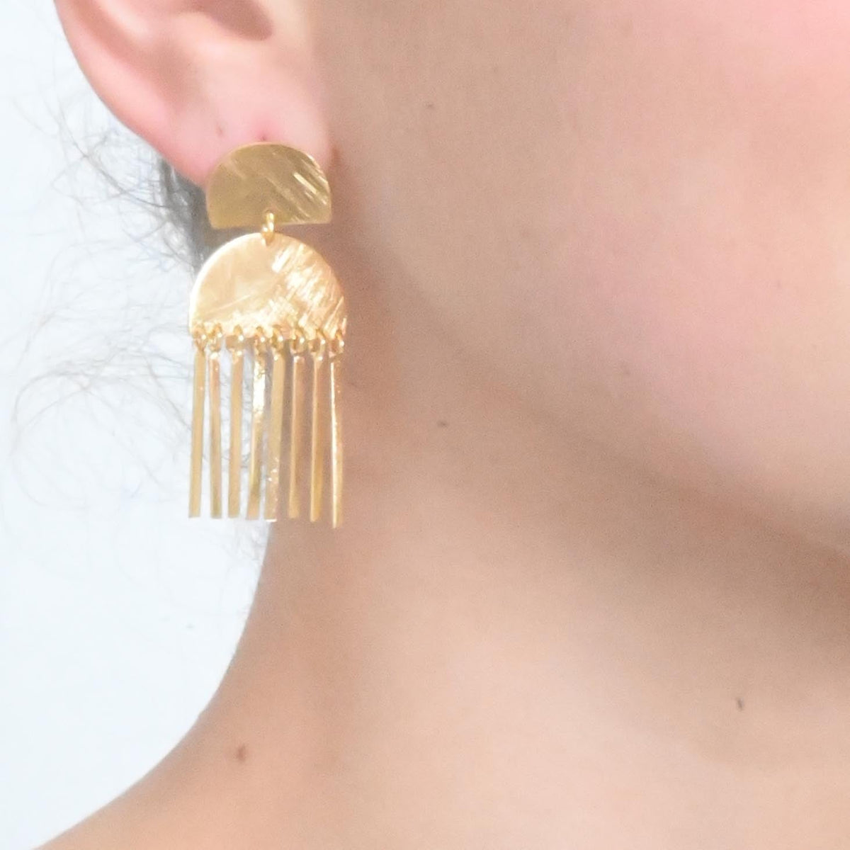 Close-up of the gold half-moon fringe earring worn on the ear