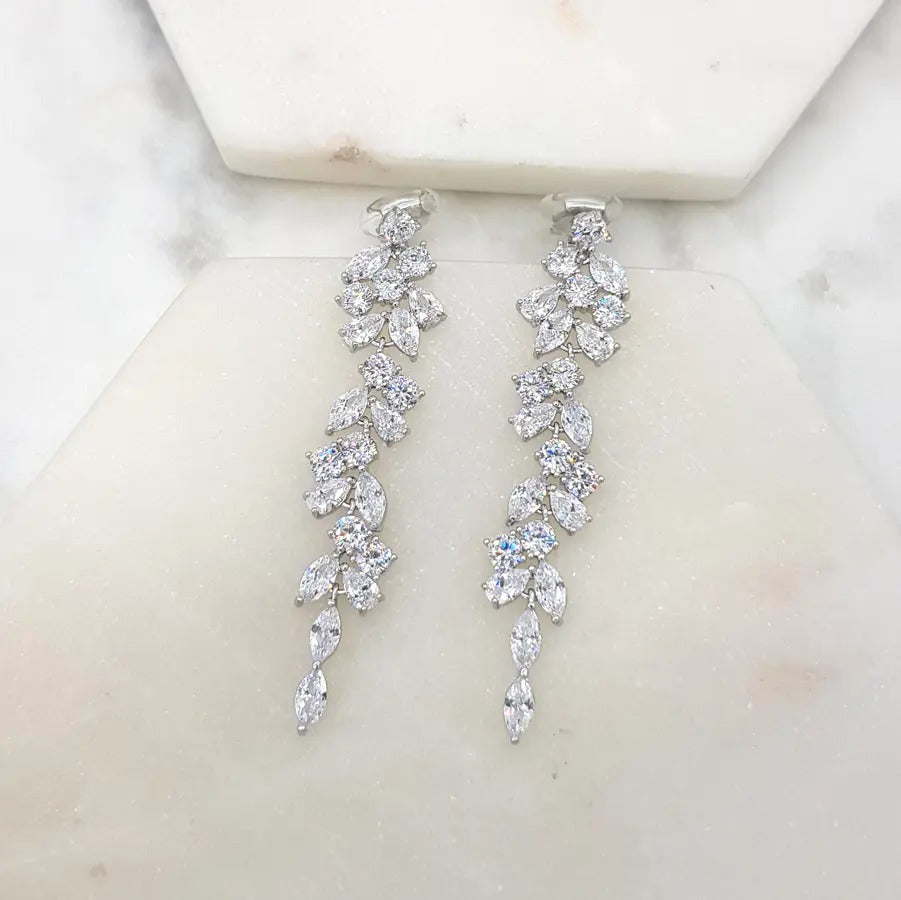 Pair of silver-tone clip-on earrings with a cascading cluster of clear marquise cubic zirconia stones, on a white marble tile
