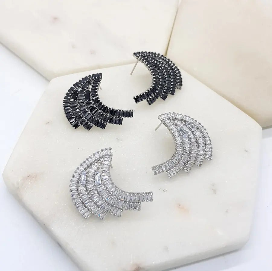 Two pairs of art-deco baguette fan earrings, one black crystal and one clear, on a marble tile
