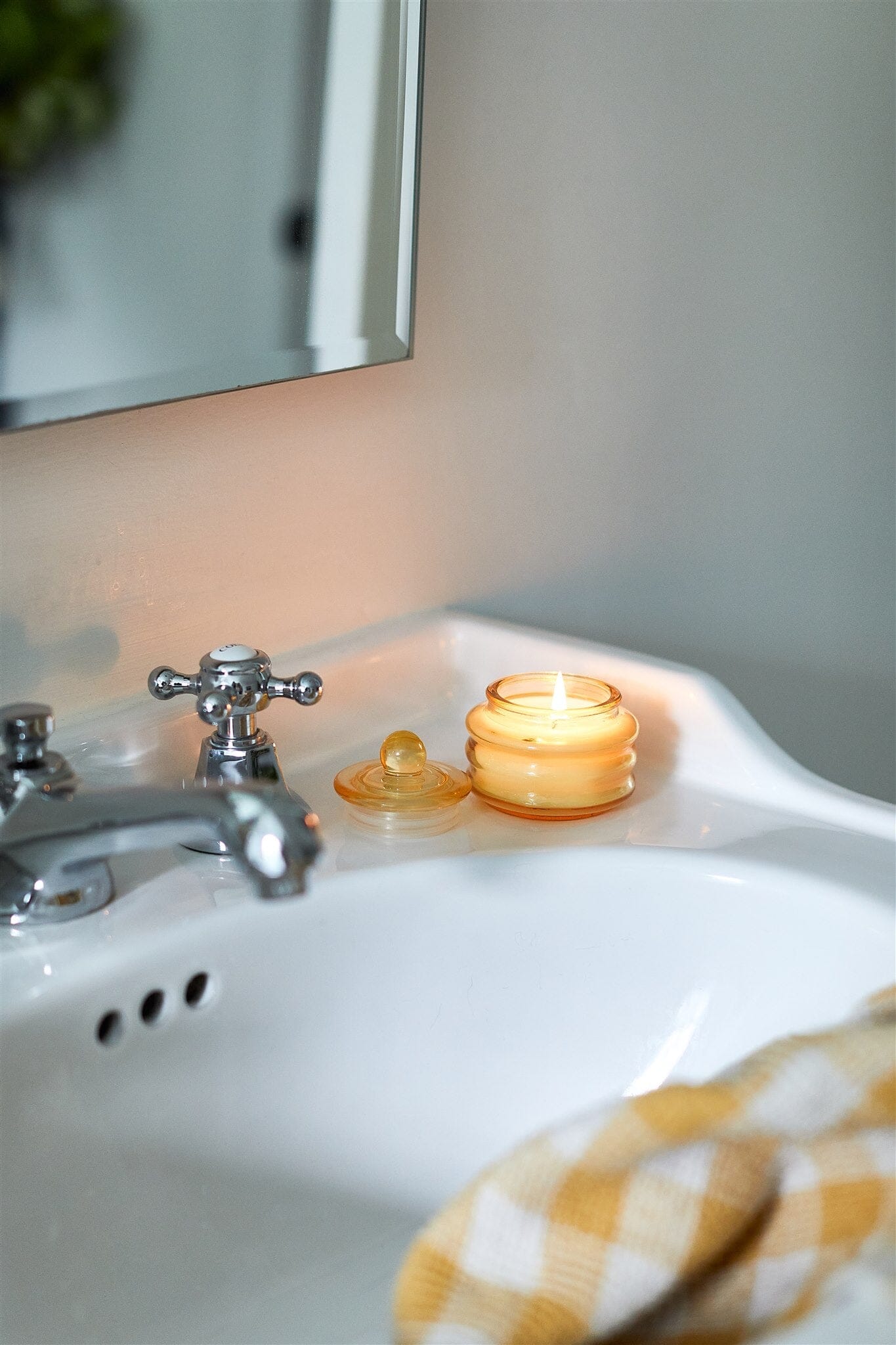 Lit Beam candle on the corner of a white basin with a gingham towel