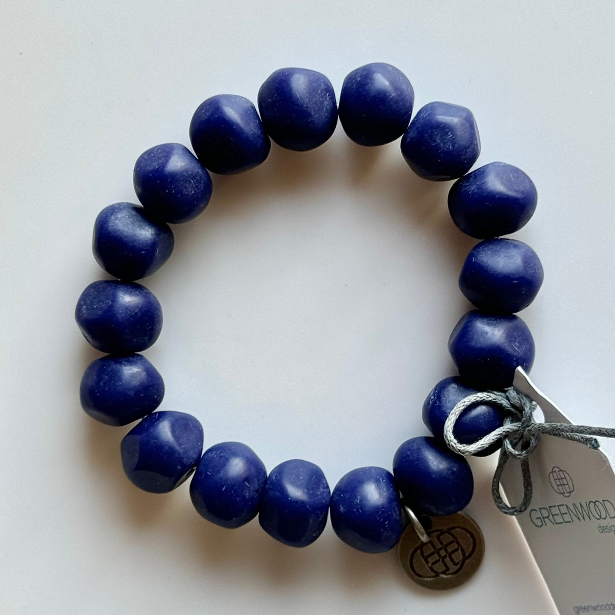 Rock bracelet in Bright Blue: a stretch bracelet of chunky deep cobalt blue resin beads with its swing tag and metal charm, laid on a pale surface.