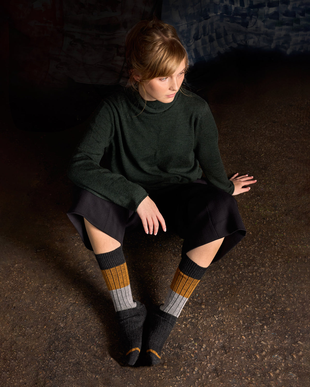 Model seated on the floor in a green knit and shorts, wearing the colour-block rib socks