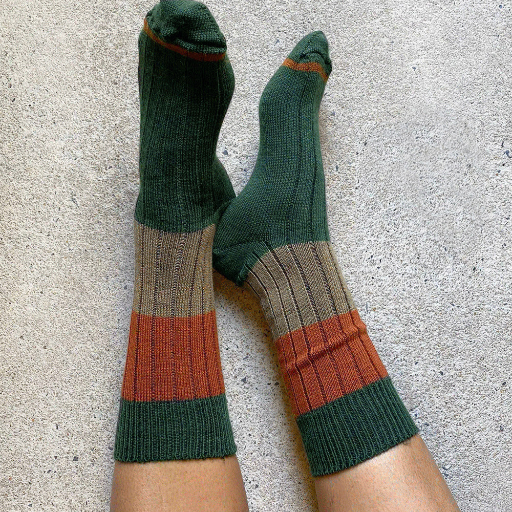 Legs crossed on concrete wearing the green, rust and khaki rib socks