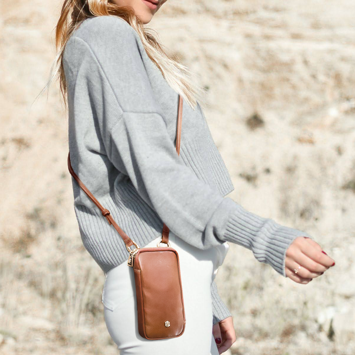 Woman in a grey knit wearing the tan leather phone pouch at her hip