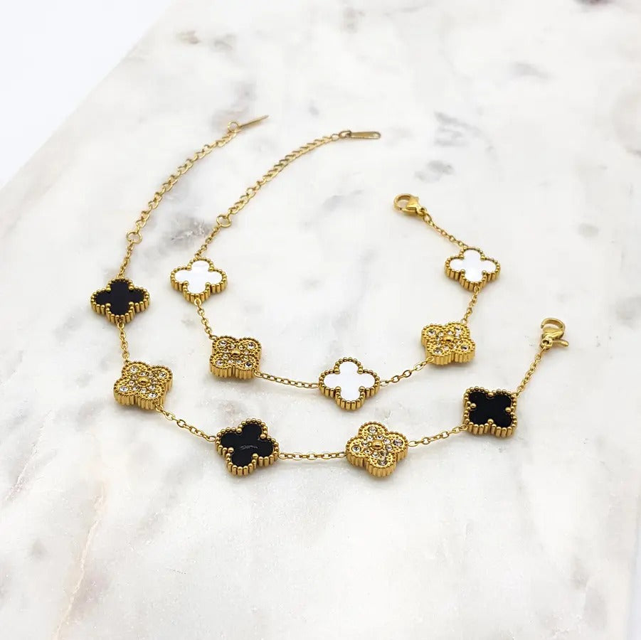 Two gold-tone clover bracelets, one with black clovers and one with white, each alternating with cubic zirconia clovers, on marble