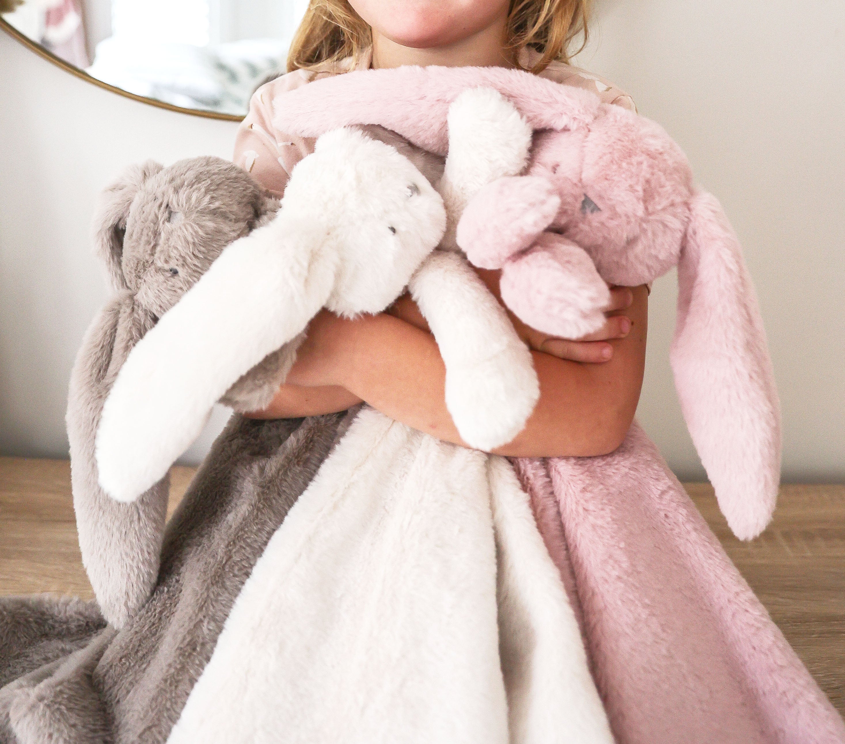 Child holding grey, white and pink bunny lovey blankets