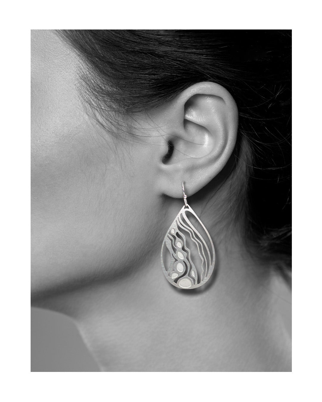 A model wearing one Flow teardrop earring, photographed in black and white