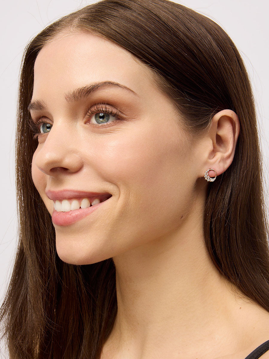 Smiling model with long brown hair wearing a small open circle stud set with sparkling clear stones