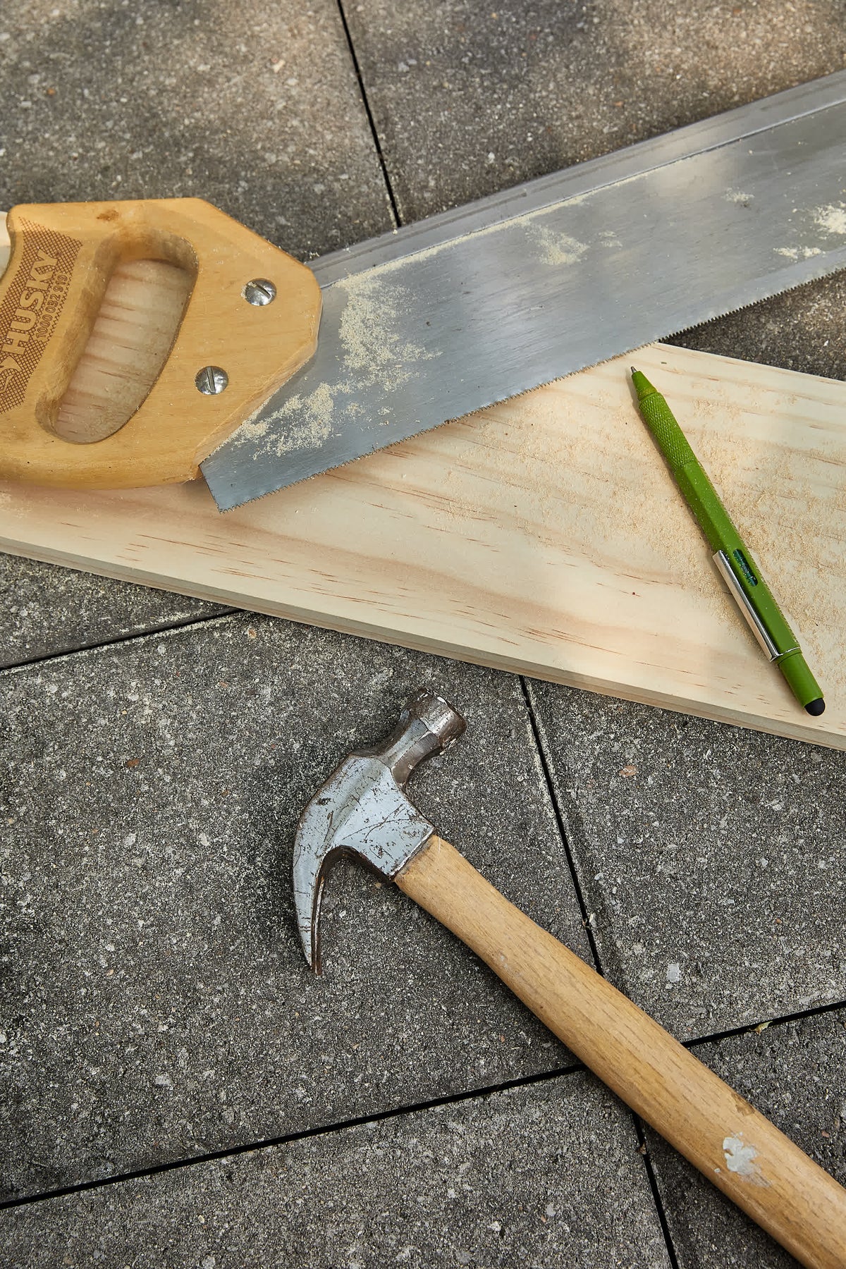 Olive green tooling pen on a timber offcut beside a hand saw and a claw hammer
