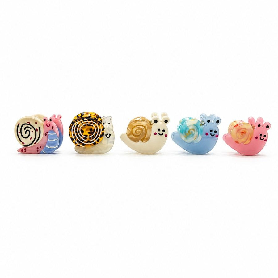 The five mini snail hair clip designs in a row, left to right: Black Swirl, Tortoiseshell-Look, Caramel, Blue and Pink