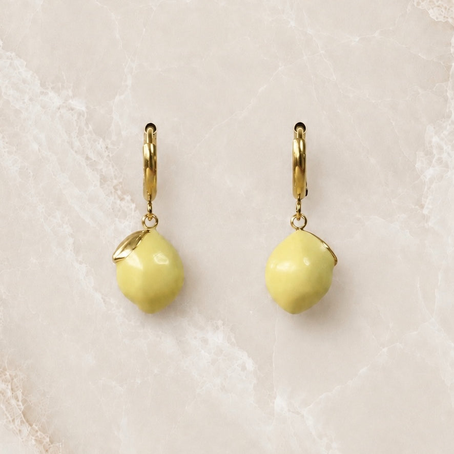 Gold huggie hoop earrings with a bright yellow enamel lemon charm hanging from each hoop