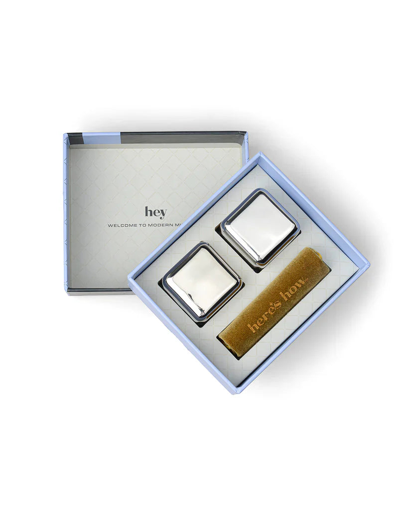 Two silver stainless steel chilling cubes and a gold velvet pouch in an open gift box