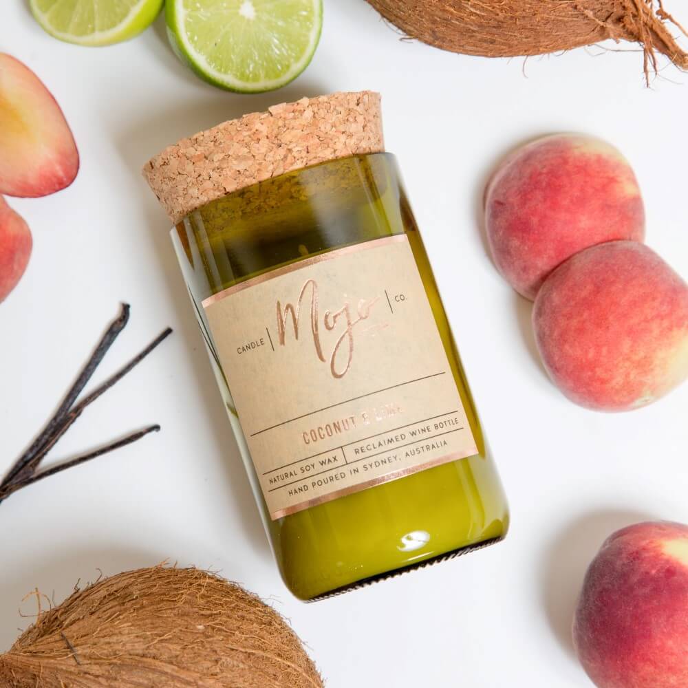 Coconut & Lime candle on white with peaches, coconut halves and vanilla pods