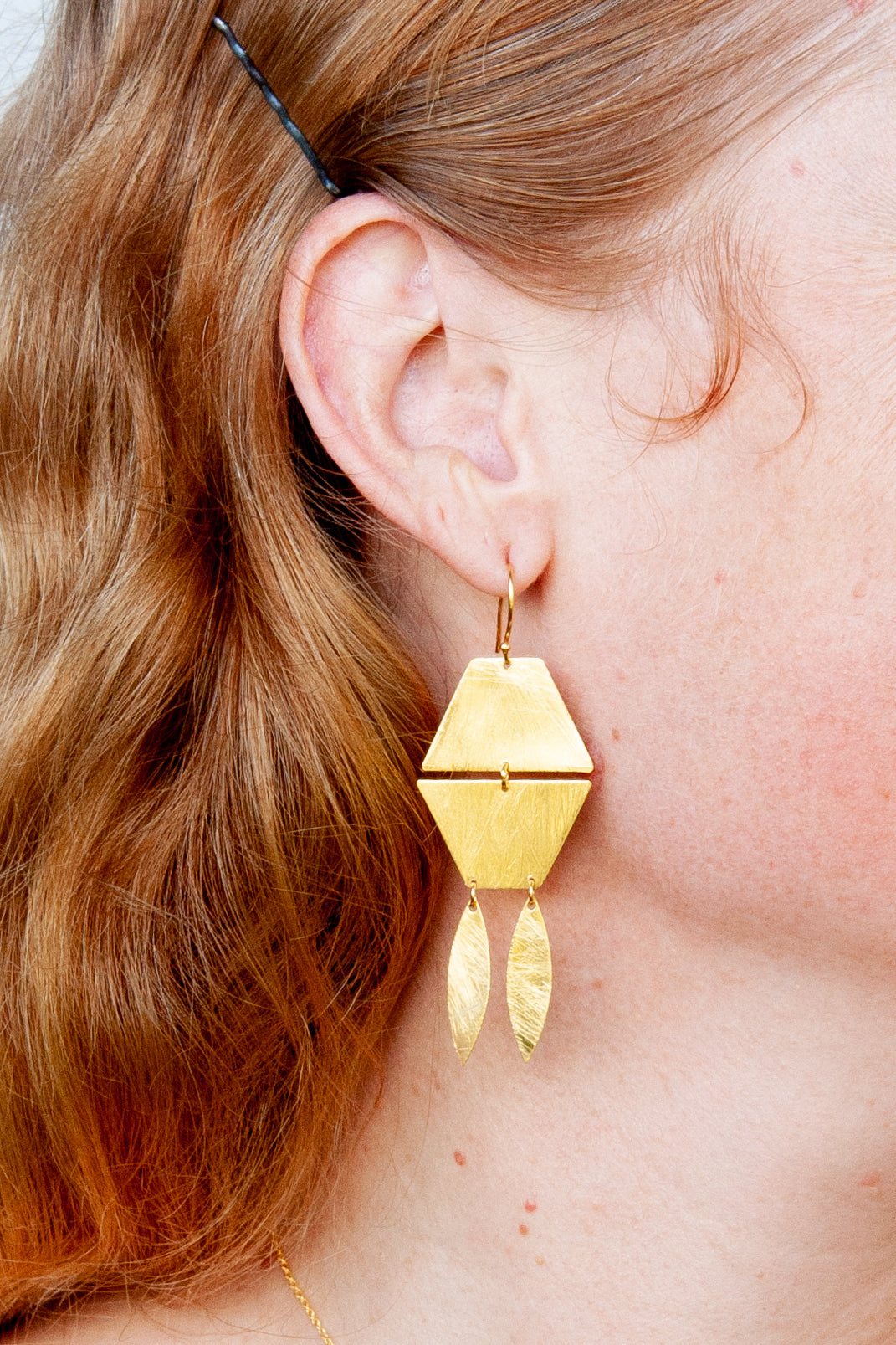 Close-up of the gold geometric drop earring worn with long red hair