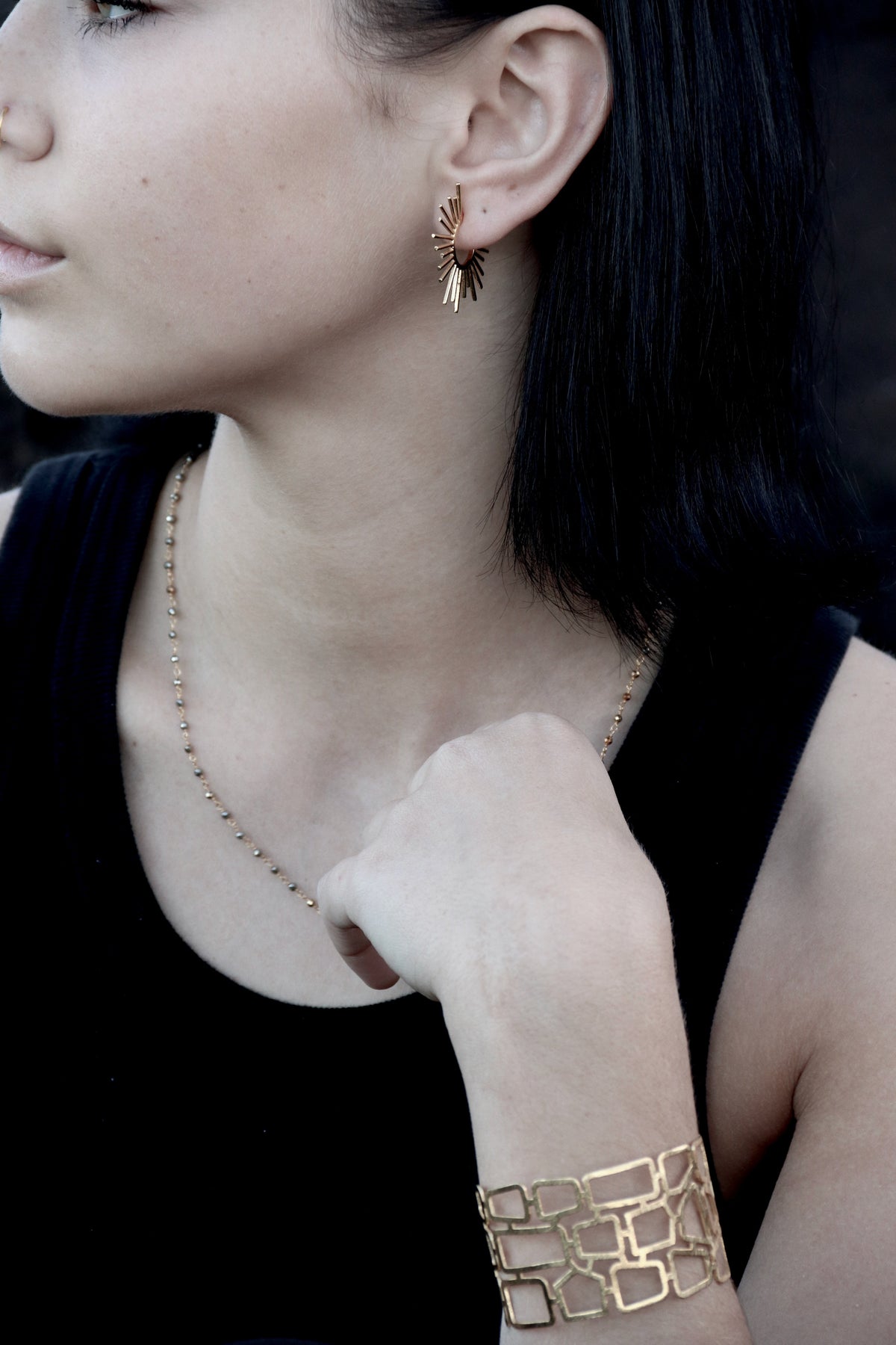 Model in a black top wearing the wide gold lattice cuff, with drop earrings and a fine beaded necklace