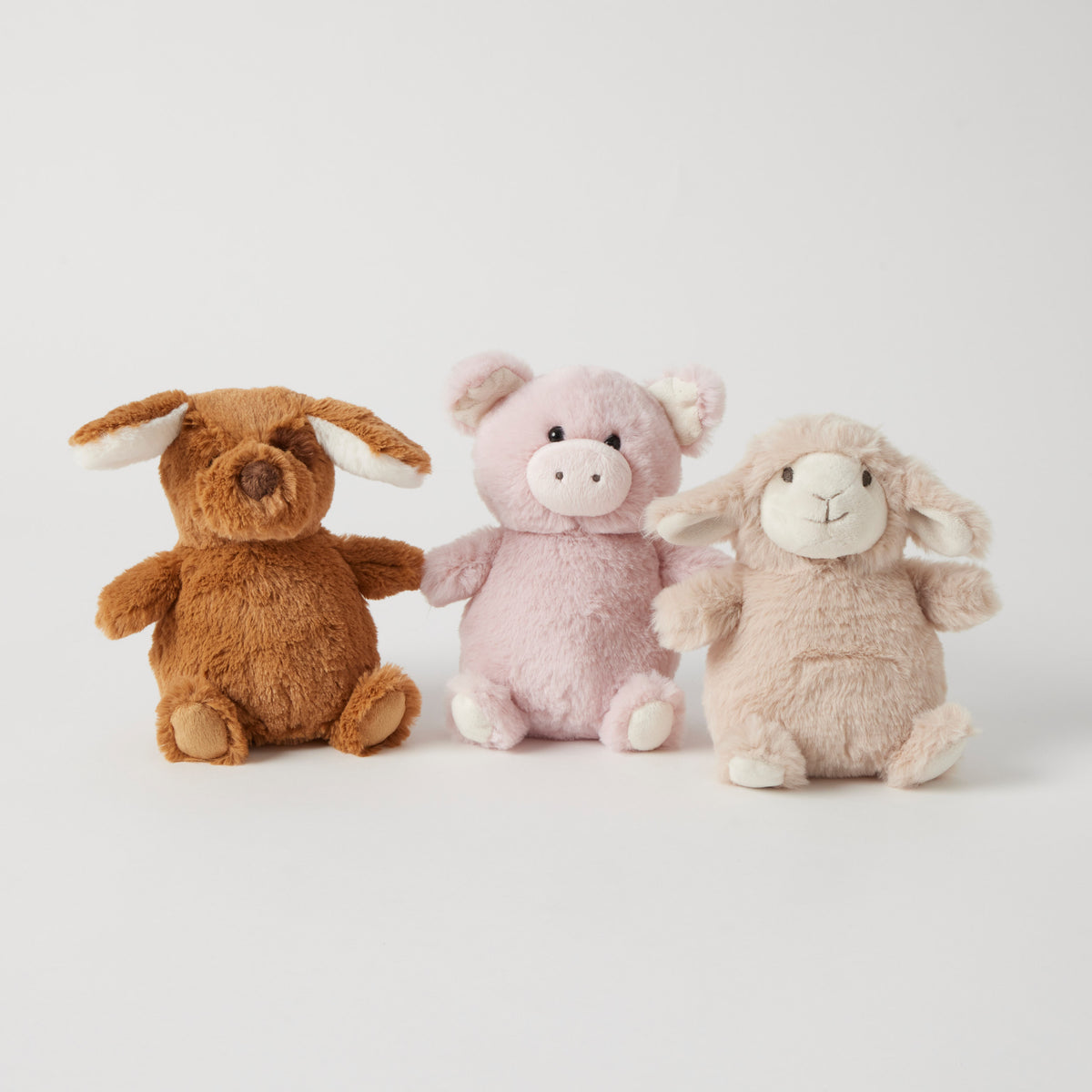 Three plush rattles sitting in a row: a brown puppy with floppy ears, a pink piglet and a cream lamb