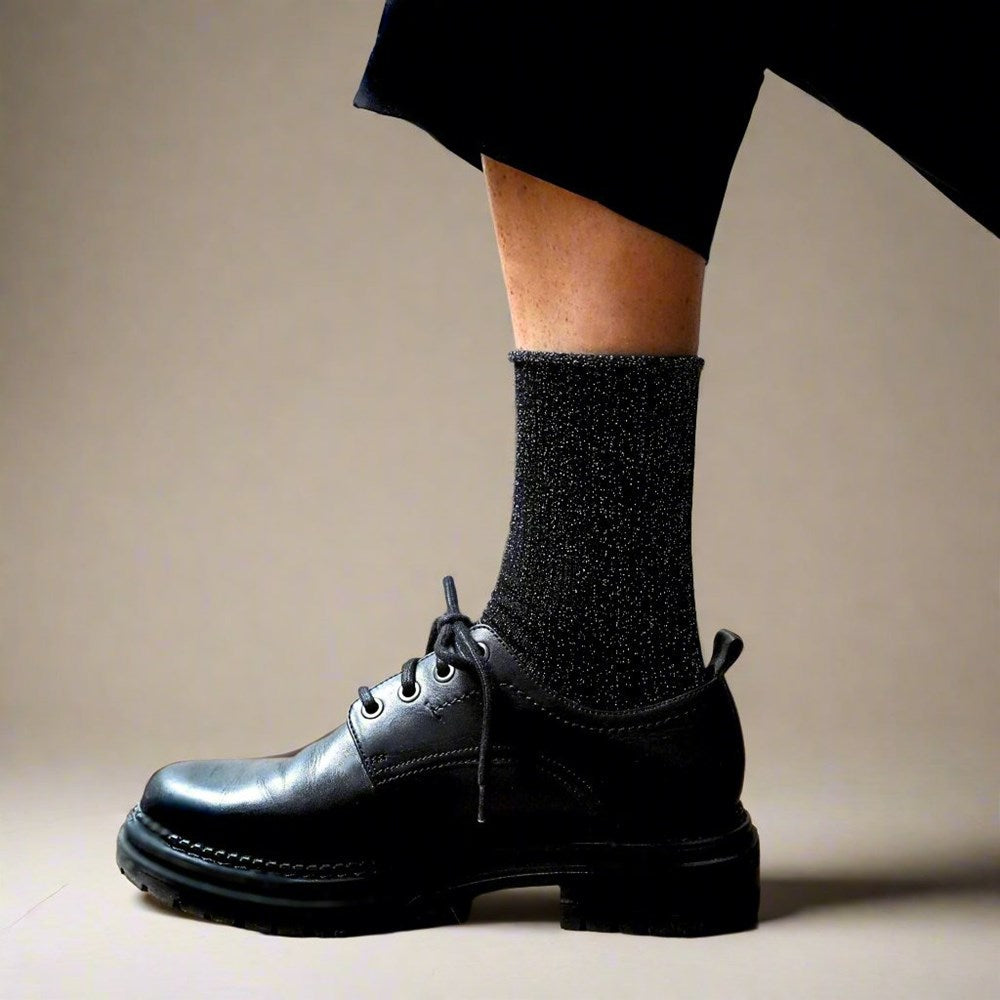 Side view of a black glitter KLUE lurex sock worn with a chunky black leather lace-up shoe
