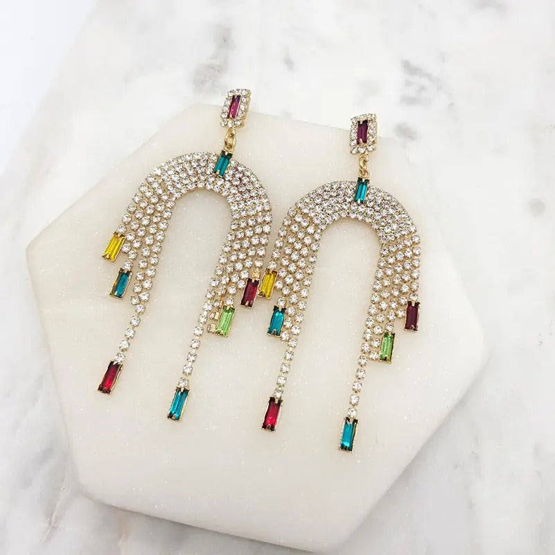 Crystal arch fringe earrings with multicoloured drops lying on a white marble tile