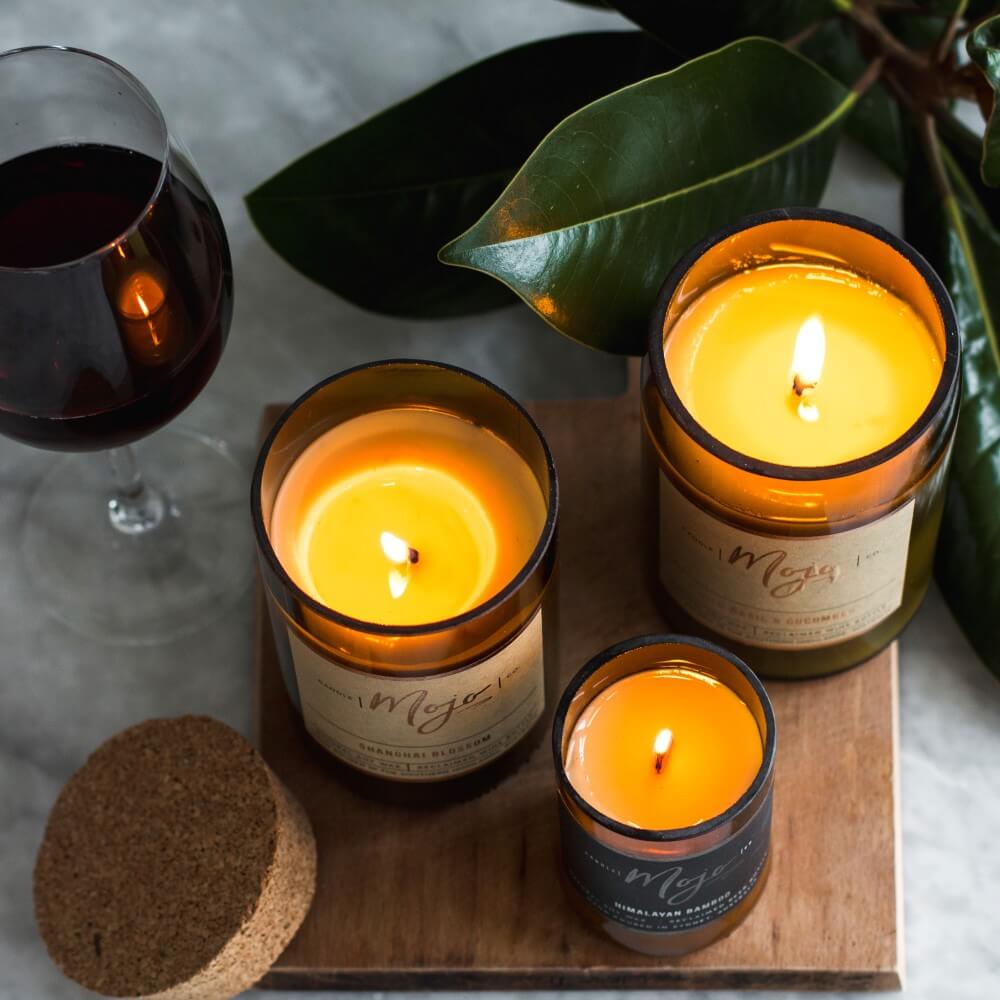 Three lit Mojo bottle candles on a timber board with a glass of red wine