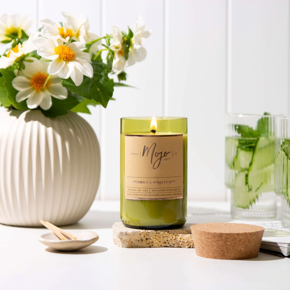 Cucumber & Muddled Mint candle burning beside white flowers and a glass of cucumber water