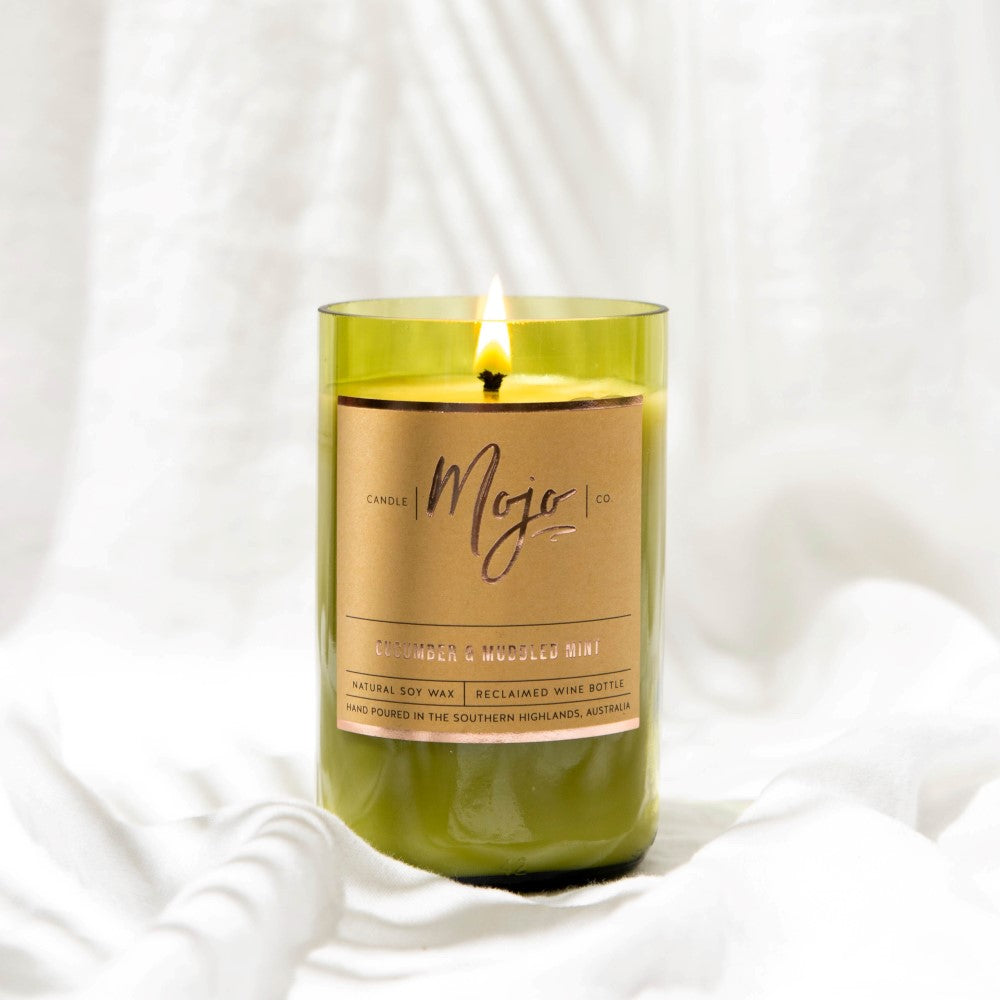 Close-up of the lit Cucumber & Muddled Mint candle in its green reclaimed wine bottle against white linen