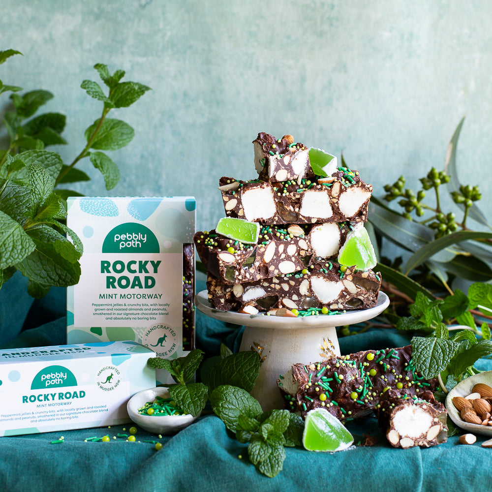 Chunks of Mint Motorway rocky road on a cake stand with marshmallow and green mint jelly, boxes and fresh mint alongside