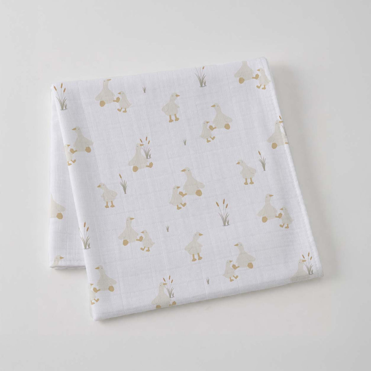 White cotton muslin wrap folded into a square, printed with small cream ducks and reeds