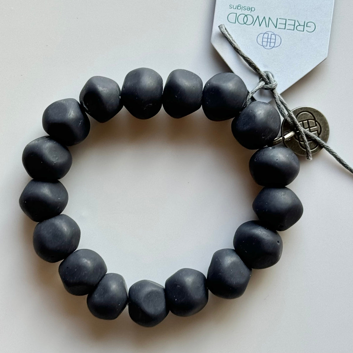 Rock bracelet in Navy: a stretch bracelet of chunky dark navy resin beads with its swing tag and metal charm, laid on a pale surface.