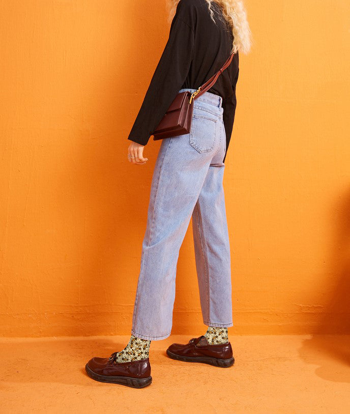 Person in pale jeans and brown loafers against a bright orange backdrop, wearing the golden bee socks.