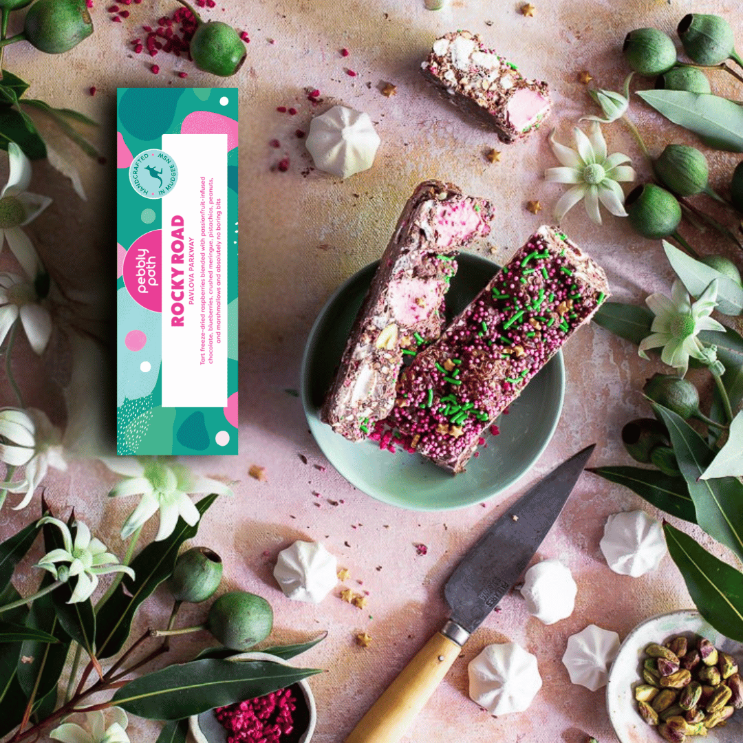 Pebbly Path Pavlova Parkway rocky road 100 g box with two slices on a green plate, mini meringues, pistachios and freeze-dried raspberries