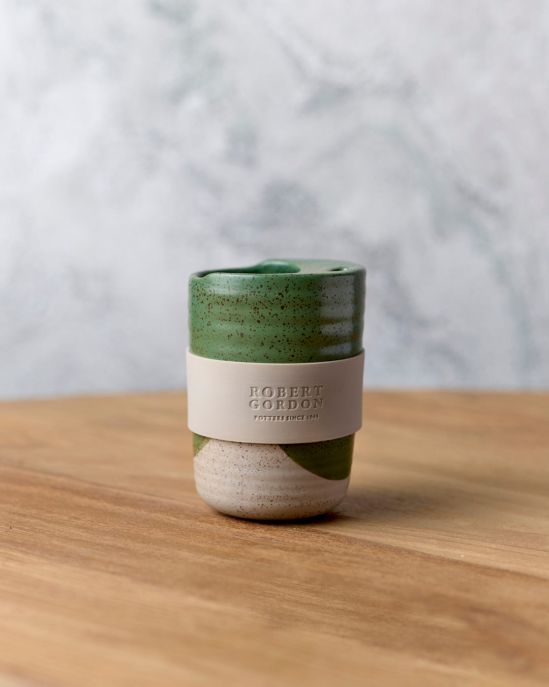 Green travel mug with beige band, close view on timber