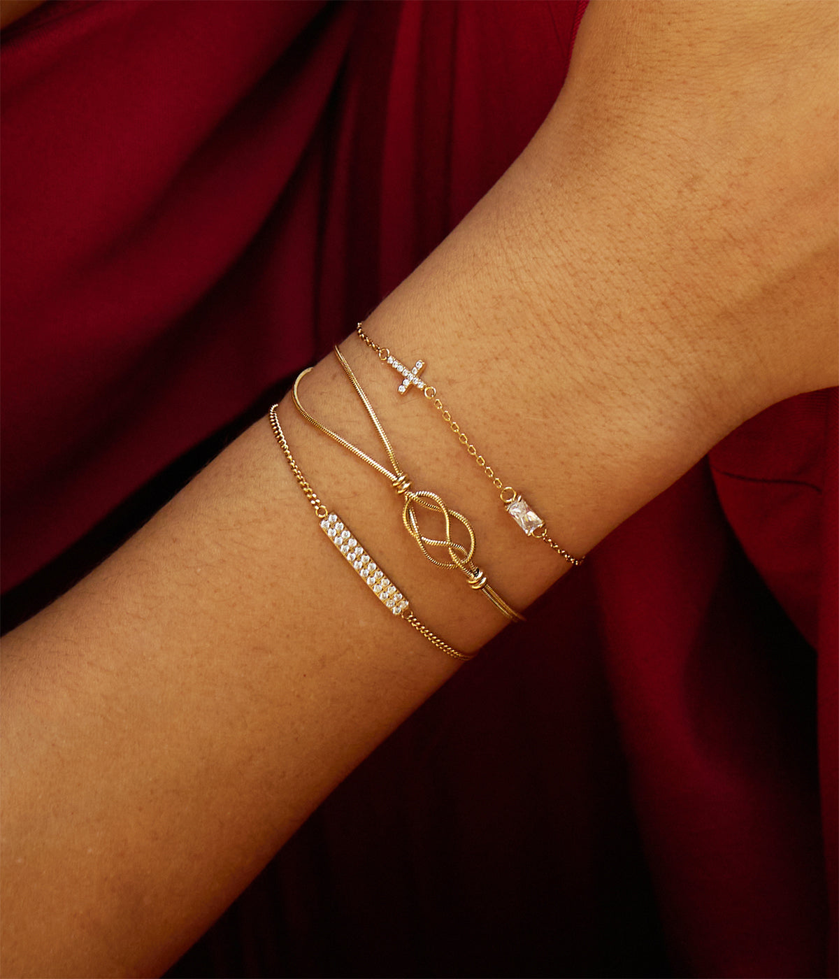 Model's wrist against red fabric wearing the double-strand bracelet with other fine gold chains
