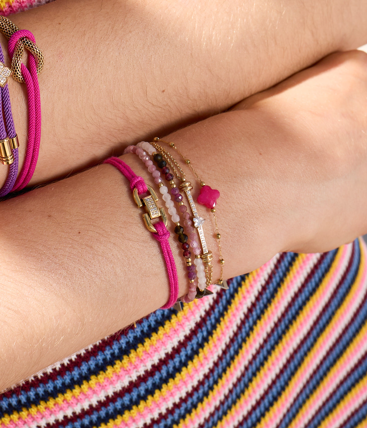 Model's wrist over striped fabric wearing stacked beaded bracelets