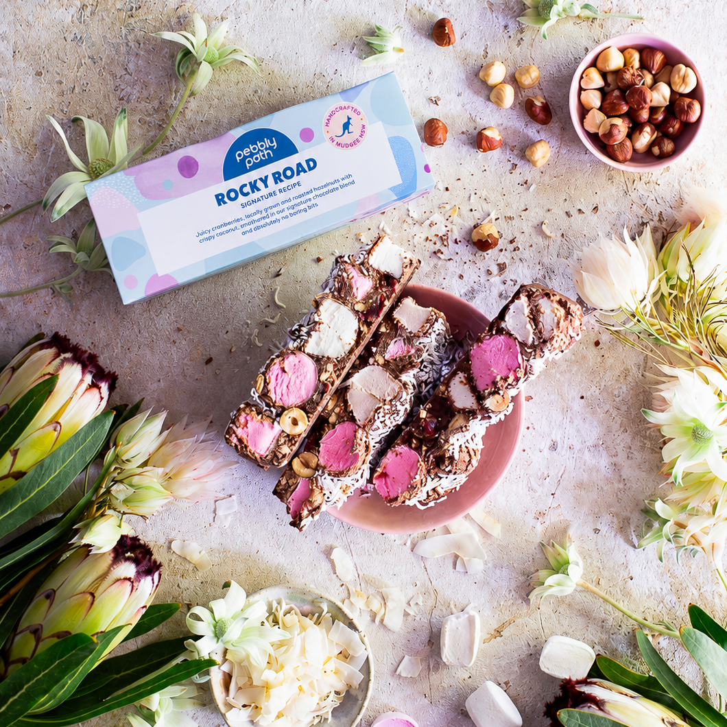 Pebbly Path Signature Recipe rocky road 100 g box with a cut slab on a pink plate, hazelnuts and coconut