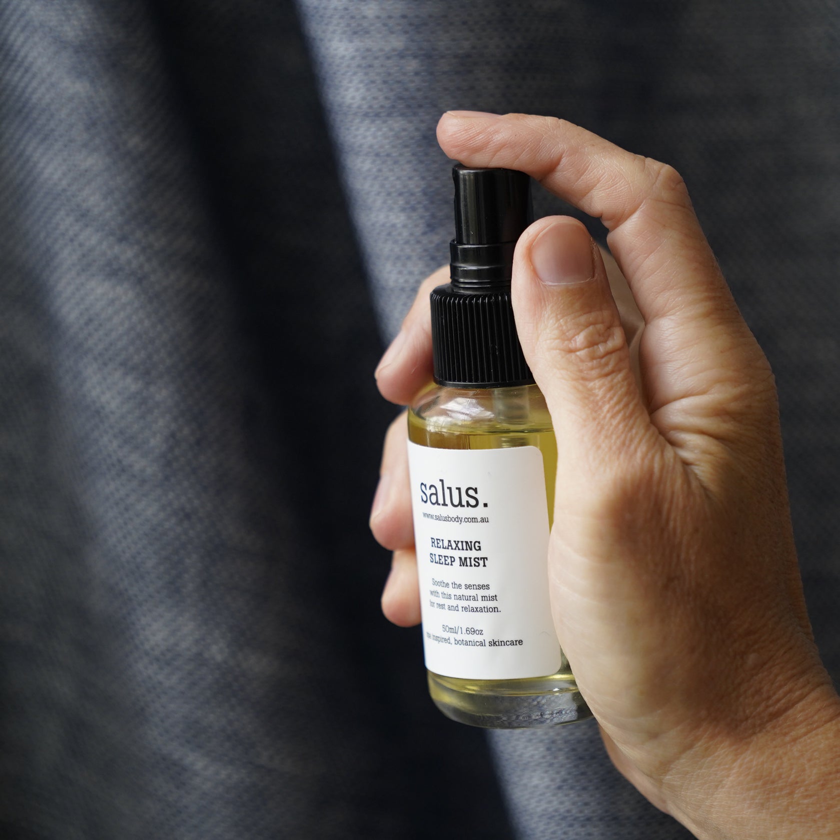 Hand holding the Salus Relaxing Sleep Mist bottle against a linen background