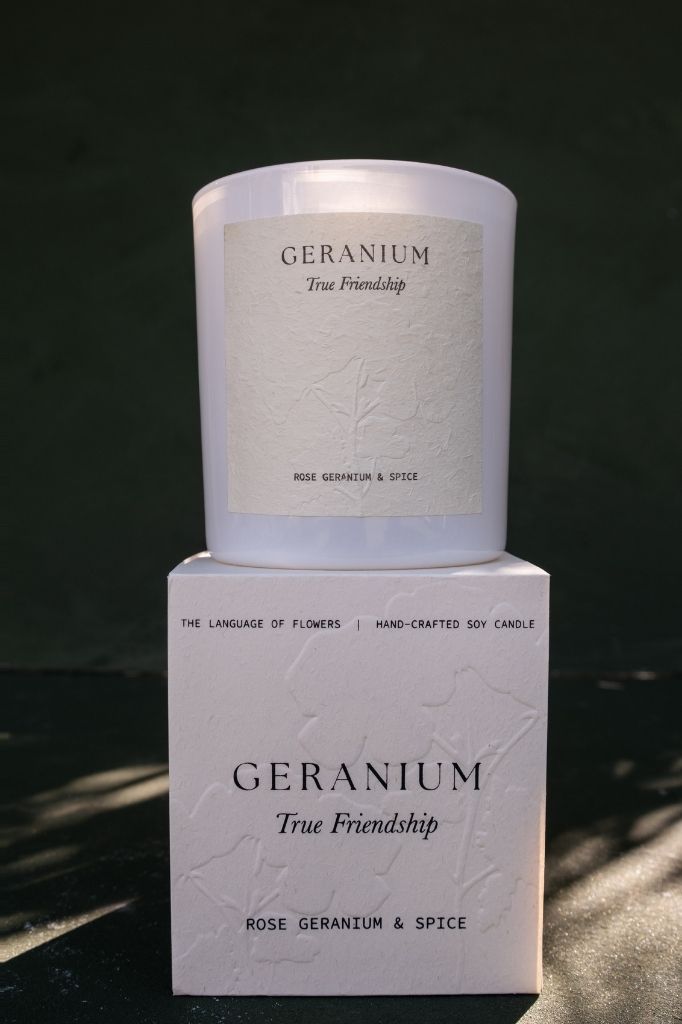 The Geranium candle standing on its box against a dark green backdrop.