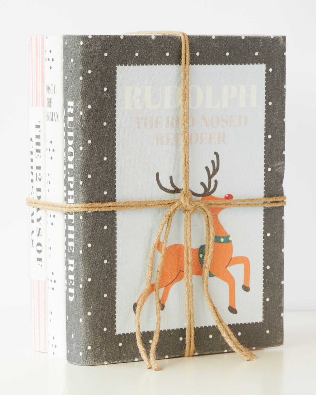 Faux vintage Christmas books standing tied with jute twine, Rudolph the Red-Nosed Reindeer on the front cover